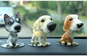 Image of three bobbleheads on a car dashboard shaped like a Husky, Labrador, and Basset Hound