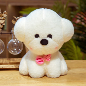 This image shows a cute Bichon Frise Stuffed Animal Plush Toy with a pink bow-tie in it's neck and  sitting on the table.