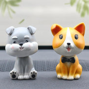 Image of two nodding bobbleheads on a car dashboard shaped like a Miniature Schnauzer and a Corgi