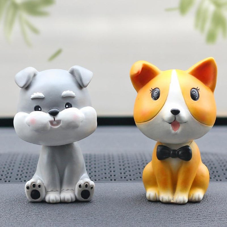 Image of two nodding bobbleheads on a car dashboard shaped like a Miniature Schnauzer and a Corgi