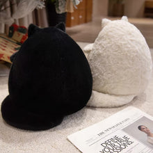 Load image into Gallery viewer, Two plush cat-shaped pillows or cushions shown from the back, one black and one white, placed on a light carpet with a magazine nearby.