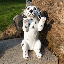 Load image into Gallery viewer, A white Dalmatian dog statue sitting on a stone slab outdoors, with its paws raised, set against a large rock and green grass in the background.