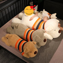 Load image into Gallery viewer, Three large plush dog pillows in beige, gray, and white, each wearing a striped sweater in orange, navy, and cream, arranged on a bed with a child lying on the white dog.