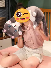 Load image into Gallery viewer, A person sitting on a bed holds a plush husky toy in front of their face, which is covered by a yellow winking emoji. The person is wearing a pink button-up shirt and white shorts in a bedroom setting.