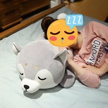 Load image into Gallery viewer, A person lying on a bed with their face covered by a yellow sleeping emoji sticker, resting on a large gray plush husky toy.
