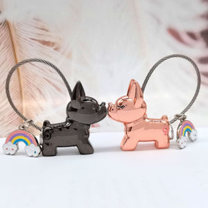Image of two metallic frenchie keychains in the color boy black and girl rose gold kissing each other