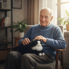 Load image into Gallery viewer, An elderly man sitting in a chair and gently petting a black-and-white cat stuffed animal in a warmly lit living room.