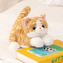 Load image into Gallery viewer, An orange and white tabby plush cat toy lying on a white bed next to a yellow book titled "BUTTER."