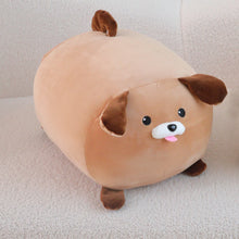 Load image into Gallery viewer, A round, plush dog-shaped cushion or pillow in light tan with darker brown ears, paws, and tail, featuring a white muzzle and pink tongue, resting on a textured light beige surface.