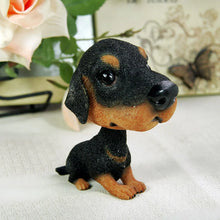 Load image into Gallery viewer, A small rottweiler dog figurine with a glossy black and tan coat, sitting on a light fabric surface with a blurred rose and decorative background.