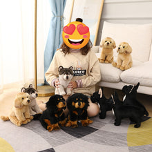 Load image into Gallery viewer, A person sitting on a patterned rug in a bright living room, surrounded by multiple plush puppy toys in different colors and breeds. 