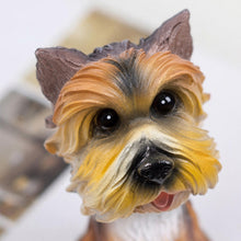 Load image into Gallery viewer, A close-up of a realistic dog figurine, likely a Yorkshire Terrier, with detailed golden-brown, black, and cream fur, large glossy black eyes, and a small pink tongue visible, set against a softly blurred light background.