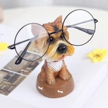 Load image into Gallery viewer, A small dog figurine wearing oversized round black-frame eyeglasses, displayed on a white surface with a blurred yellow flower in the background.