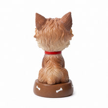 Load image into Gallery viewer, A small dog figurine shown from the back, with tan and cream fur, a red collar, and a brown base decorated with white bone shapes, photographed on a plain white background.