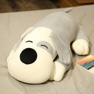 This image shows an adorable grey colored Basset Hound Stuffed Animal Plush Pillow lying on a bed.