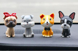 Image of four nodding bobbleheads on a car dashboard shaped like a girl Pug, Miniature Schnauzer, Corgi, and Boston Terrier
