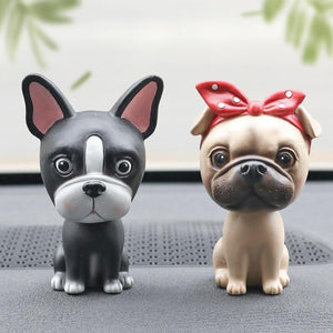 Image of two nodding bobbleheads on a car dashboard shaped like a Boston Terrier and a girl Pug